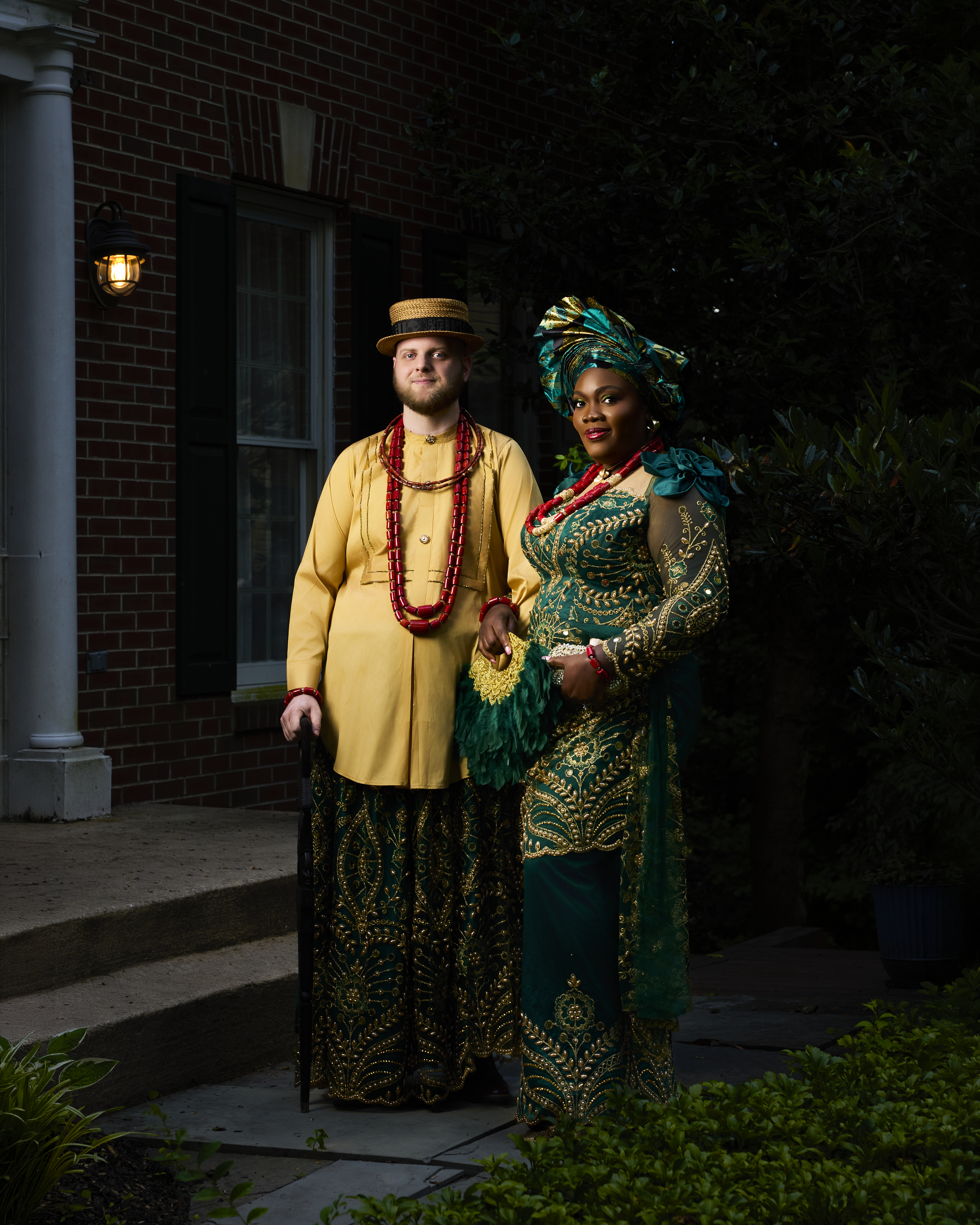 Couple in traditional attire with coral beads outside a brick home
